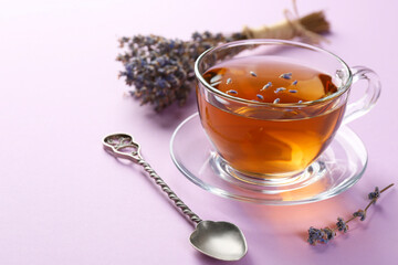 Aromatic lavender tea in glass cup, spoon and dry flowers on pink background, closeup. Space for text