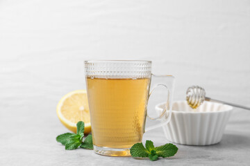 Aromatic mint tea in glass cup, fresh leaves and lemon on light gray table against white background