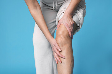 Woman suffering from pain in her knee on light blue background, closeup