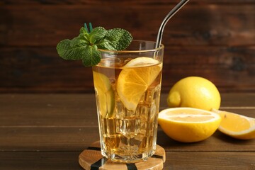Refreshing iced tea with slices of lemon, lime, mint and drinking straw on wooden table, closeup