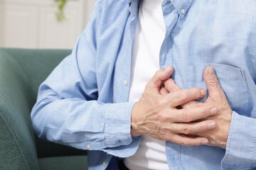 Heart attack. Senior man suffering from pain in chest on sofa at home, closeup