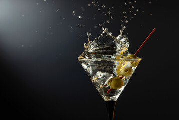 Glass of classic dry martini cocktail with green olives on a black background.