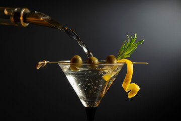 Classic dry martini cocktail with green olives, lemon peel, and rosemary on a black background.