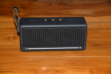 A rectangle black Bluetooth portable speaker on a wooden table