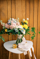 Bride bouquet stands on a white chair near a box with rings against a wooden wall