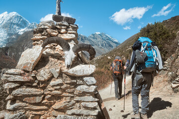 Group hikers with backpacks in mountains pass by an identifying ancient stupa made of flat stones...