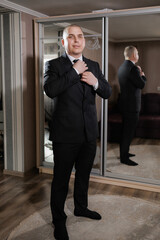 A man in a suit is getting ready to tie his tie. He is standing in front of a mirror