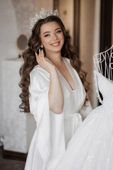A woman in a white gown is standing in front of a dresser with a white gown hanging on it