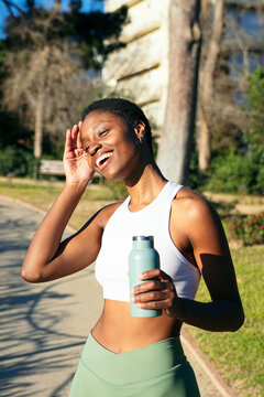 Happy sporty black woman drinking water after training outdoors in a park