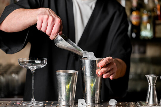 A bartender skillfully prepares a cocktail using a shaker, ice, and a glass, showcasing the art of mixology in a stylish bar setting.
