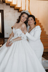 A woman in a wedding dress is posing for a picture with another woman. The bride is wearing a tiara...