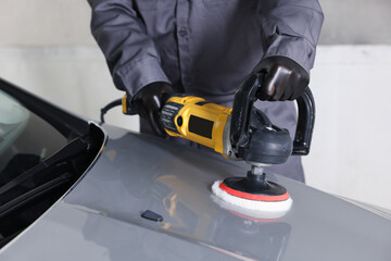 Man polishing car hood with orbital polisher indoors, closeup
