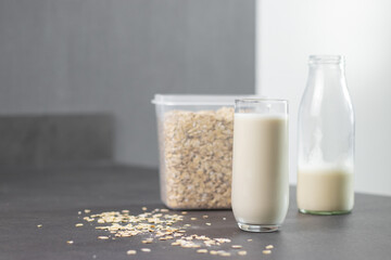 A glass of oat milk and oatmeal in a box on grey kitchen table. Vegan and non-dairy alternative milk