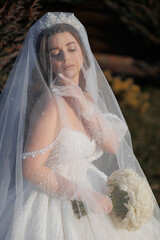 A woman in a wedding dress is wearing a veil and holding a bouquet. She is standing in a field, and...