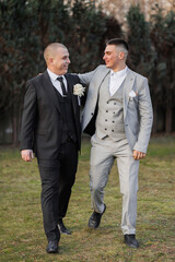 Two men in suits are walking together, one of them wearing a tie with a flower on it