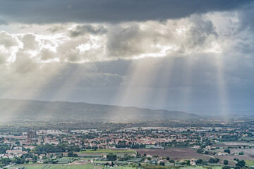 The sky is cloudy and the sun is shining through the clouds in Assisi city in Umbria Italia