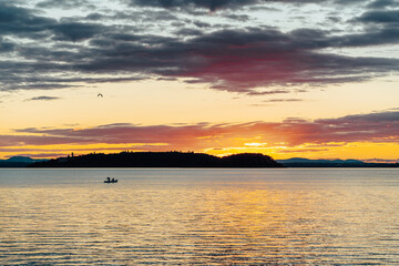 A large body of water with a sun shining on it evening on Lake Trasimeno in the region of Umbria Italy. There's a small boat floating in the distance.