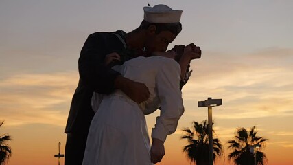 Close-up view of the iconic sailor and nurse statue in Civitavecchia near Rome, Italy, set against a beautiful Mediterranean sunset. A tribute to a historic moment with warm evening sky tones.