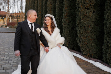 A bride and groom are walking down a path in a snowy setting. The bride is wearing a white dress...