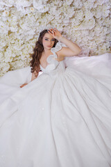 Fototapeta premium A woman is wearing a white dress with a tiara on her head. She is sitting on a bed and looking at the camera. The dress is long and has a lot of sparkles, giving it a glamorous and elegant appearance