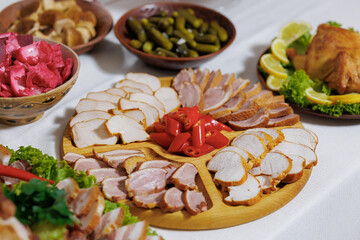 A table with a variety of meats and vegetables, including chicken, ham, and pickles. The table is set for a meal, and the food looks delicious