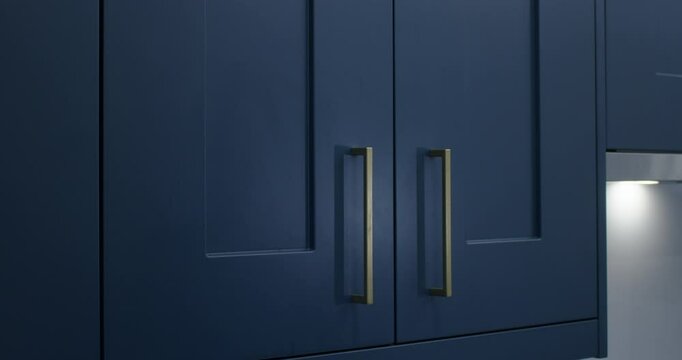 Spying kitchen cleaner onto blue modern shaker kitchen cabinet doors to clean them with microfiber cloth,