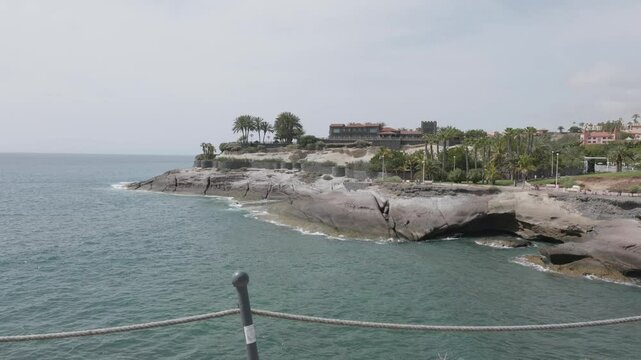 Rocks, palm trees and houses on the coast of Playa del Duque, Los Cristianos, Tenerife, Spain.