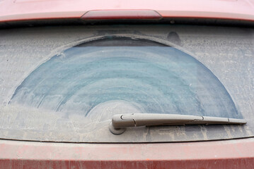 Close-up of car wiper blade and windshield covered in dust with wiper blade cleaning pattern, need for routine maintenance to ensure road safety and clear vision..