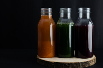 Bottles of carrot, spinach and beetroot smoothies on a dark rustic background. Healthy natural drinks