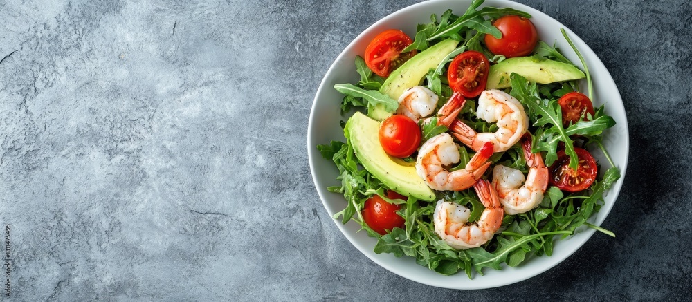 Poster fresh avocado shrimp salad in round white bowl with arugula and cherry tomatoes on gray stone surfac