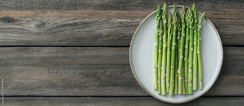 Poster Fresh green asparagus arranged neatly on a round white plate atop a rustic wooden surface with ample negative space for text.