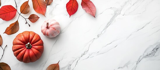 Chic autumn flatlay featuring vibrant red and orange leaves and two pumpkins on a white marble surface with ample copy space on the right.