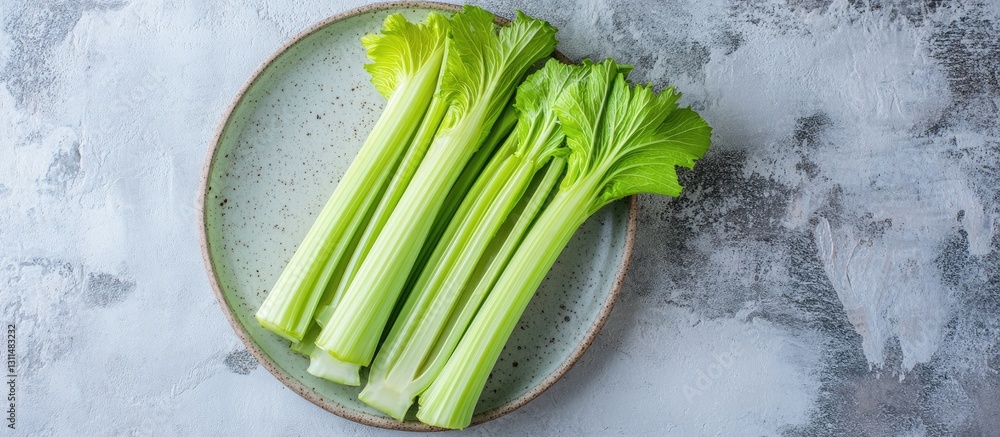 Poster Fresh green celery stalks arranged neatly on a textured light gray stone plate; top view flat lay with ample negative space for text.