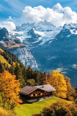 Fototapeta premium Stunning mountain landscape with an alpine chalet surrounded by vibrant autumn colors and towering snow-capped peaks in the foreground of a bright blue sky