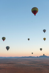 Hot air balloons float above an open landscape at sunrise, with mountains in the background. The sky transitions from deep blue to warm hues of dawn.