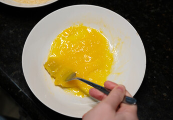 Female hands beat eggs with fork in a bowl, homemade schnitzel cooking process closeup