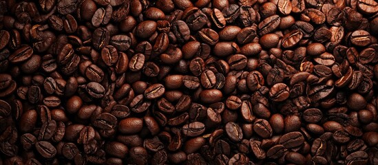 Fototapeta premium Aromatic roasted coffee beans in rich brown tones, densely packed in a close-up view creating a textured background suitable for beverage themes.