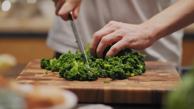 Hand von Koch zerschneidet Brokkoli in kleine St&uuml;cke in K&uuml;che auf Holzplatte Gesunder Lifestyle mit gesunder Ern&auml;hrung, leckerem und gesundem Essen im Close up