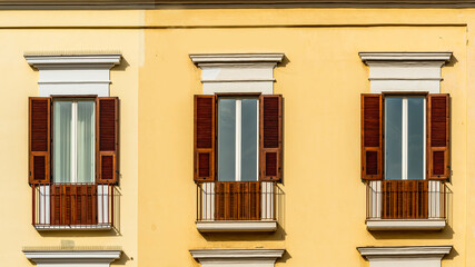Fototapeta premium old yellow facade of house with three brown vintage wooden windows in retro italian european style