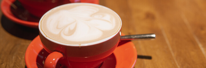 Artistic latte creations served in red cups on a wooden table. A perfect representation of a cozy cafe atmosphere for coffee lovers.