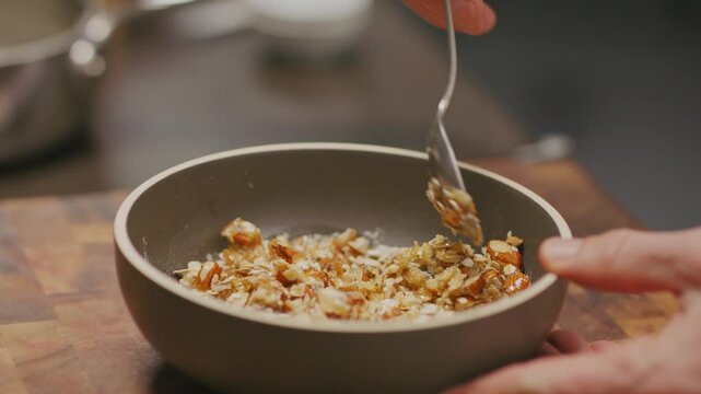 Hand von Koch bereitet ein Veganes, gesundes, Fr&uuml;hst&uuml;ck, mit N&uuml;ssen und Honig durch r&uuml;hren seines L&ouml;ffels in einer Sch&uuml;ssel, auf Holz vor