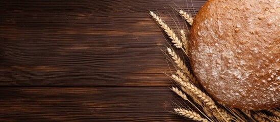 Round buckwheat bread placed on a dark wooden background with scattered wheat stalks on the bottom right side creating a rustic appearance