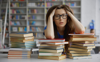 Tired woman sitting front of huge stack of book in library