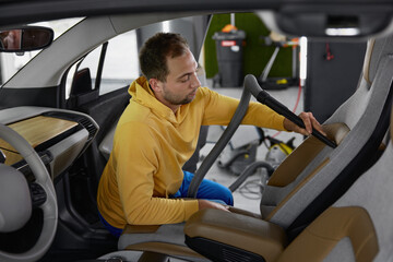 Male master vacuuming car interior from dust using professional equipment