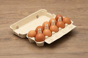 A carton containing ten fresh brown eggs is placed on a wooden surface, showcasing its natural hue...