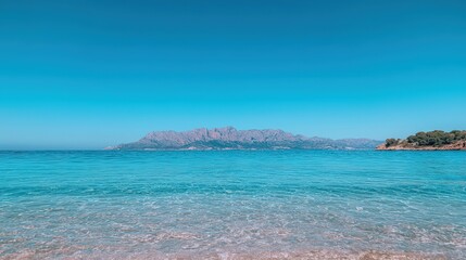 Clear turquoise water, sandy beach, mountains in distance under a vibrant blue sky.