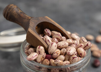 Glass jar full of dried pinto beans with scoop on gray closeup. Traditional Latin American legumes