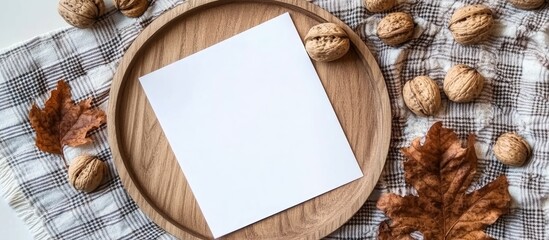 Minimalist autumn still life featuring a blank white paper on a wooden tray surrounded by walnuts and dry leaves on a soft plaid background