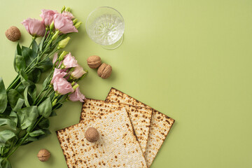 Passover items arranged with matzoh, pink flowers, walnuts, and a wine glass on green background,...