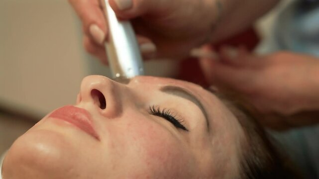 Woman receiving facial massage from skilled therapist in beauty salon. Microcurrent Therapy, Ultrasound Facial Massage. Face treatment, skin nourishment, rejuvenation cosmetology for adult lady